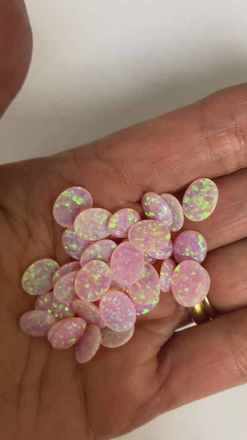 Multiple 6x8mm reconstructed pink fire opal oval cabochons showing consistent candy pink color and play-of-color